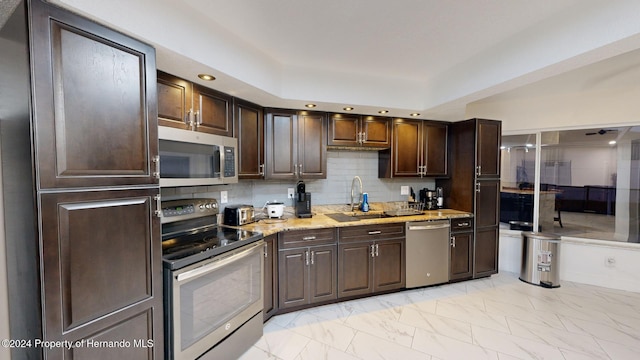 kitchen featuring dark brown cabinetry, sink, stainless steel appliances, light stone counters, and decorative backsplash