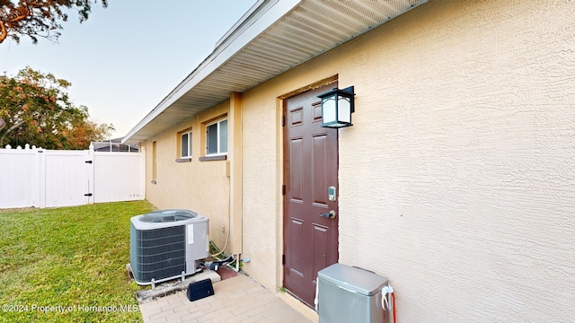 view of exterior entry featuring central AC unit and a yard