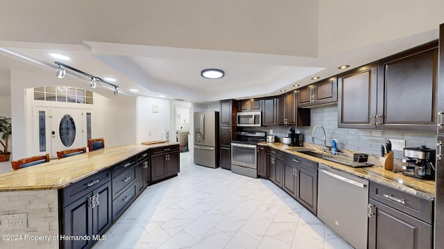 kitchen with backsplash, sink, light stone countertops, dark brown cabinets, and stainless steel appliances