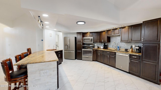 kitchen featuring sink, kitchen peninsula, decorative backsplash, a breakfast bar, and appliances with stainless steel finishes