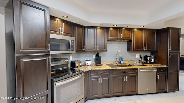 kitchen featuring backsplash, light stone counters, dark brown cabinets, stainless steel appliances, and sink