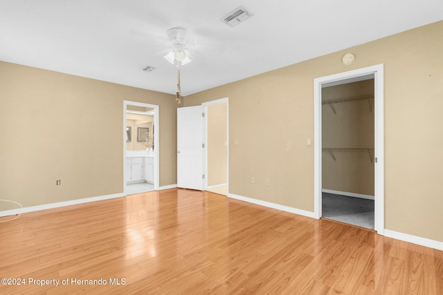 unfurnished bedroom featuring a walk in closet, ensuite bath, light hardwood / wood-style flooring, and ceiling fan