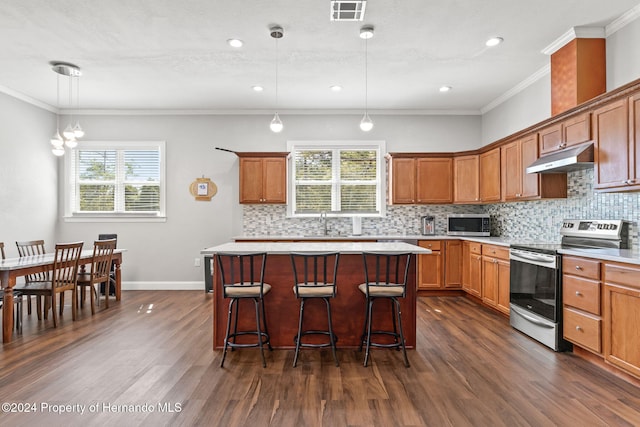 kitchen with a center island, stainless steel appliances, dark hardwood / wood-style flooring, crown molding, and pendant lighting