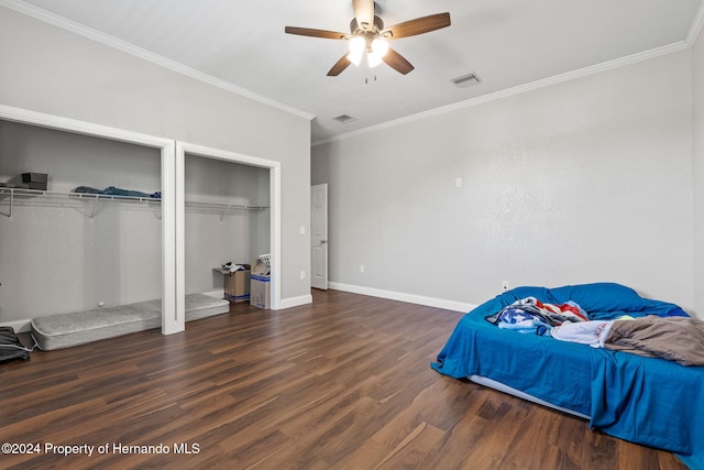 bedroom with ceiling fan, dark hardwood / wood-style flooring, crown molding, and two closets