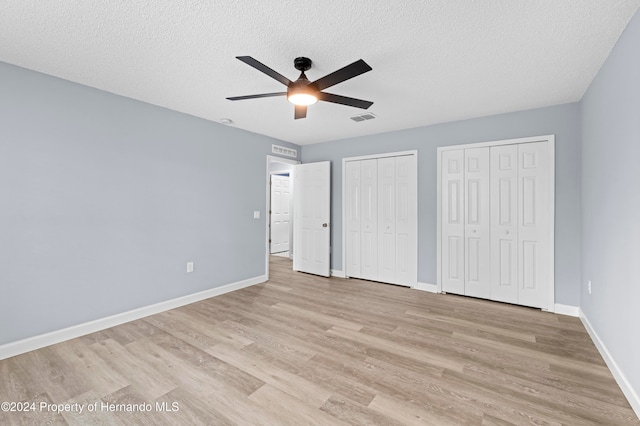 unfurnished bedroom featuring two closets, a textured ceiling, light hardwood / wood-style floors, and ceiling fan