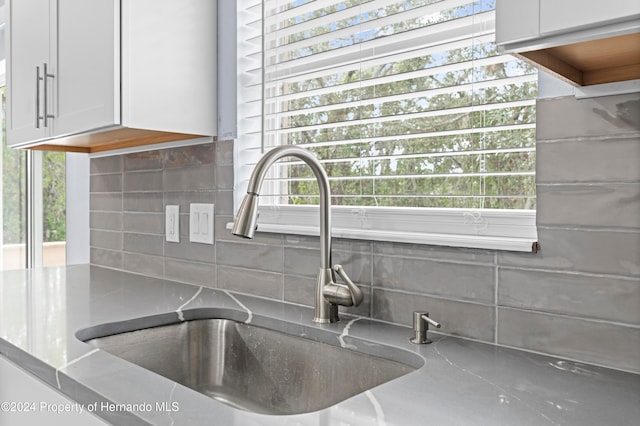 details with backsplash, light stone countertops, white cabinetry, and sink