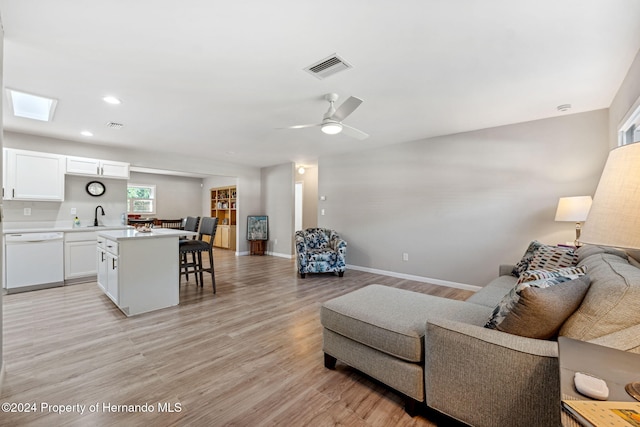 living room featuring a skylight, light hardwood / wood-style floors, ceiling fan, and sink