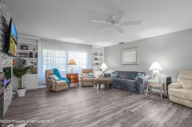 living room featuring hardwood / wood-style flooring, ceiling fan, built in features, and a textured ceiling