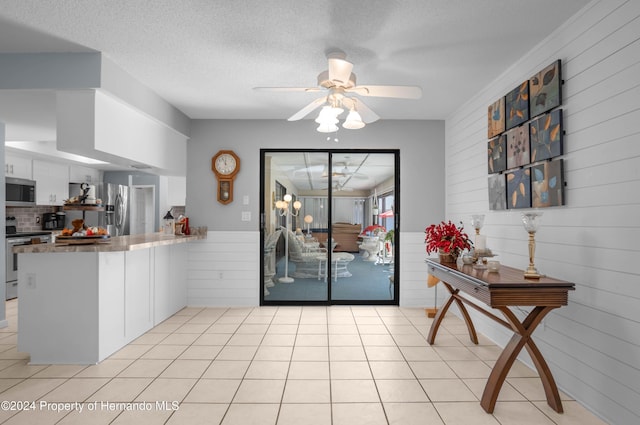 kitchen with kitchen peninsula, wooden walls, white cabinets, and appliances with stainless steel finishes