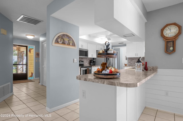 kitchen with kitchen peninsula, tasteful backsplash, stainless steel appliances, light tile patterned floors, and white cabinetry