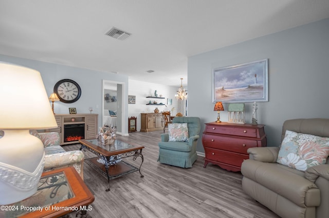 living room featuring light hardwood / wood-style floors, a brick fireplace, and a notable chandelier