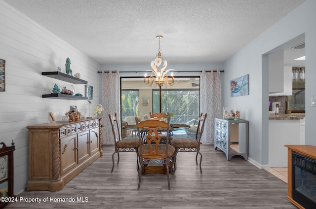 dining space with a chandelier, wood-type flooring, a textured ceiling, and wood walls