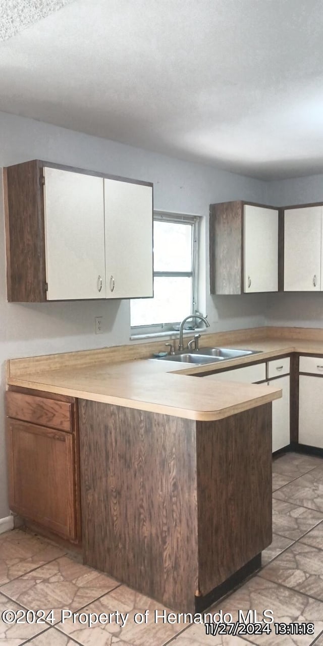 kitchen with a textured ceiling, white cabinetry, and sink