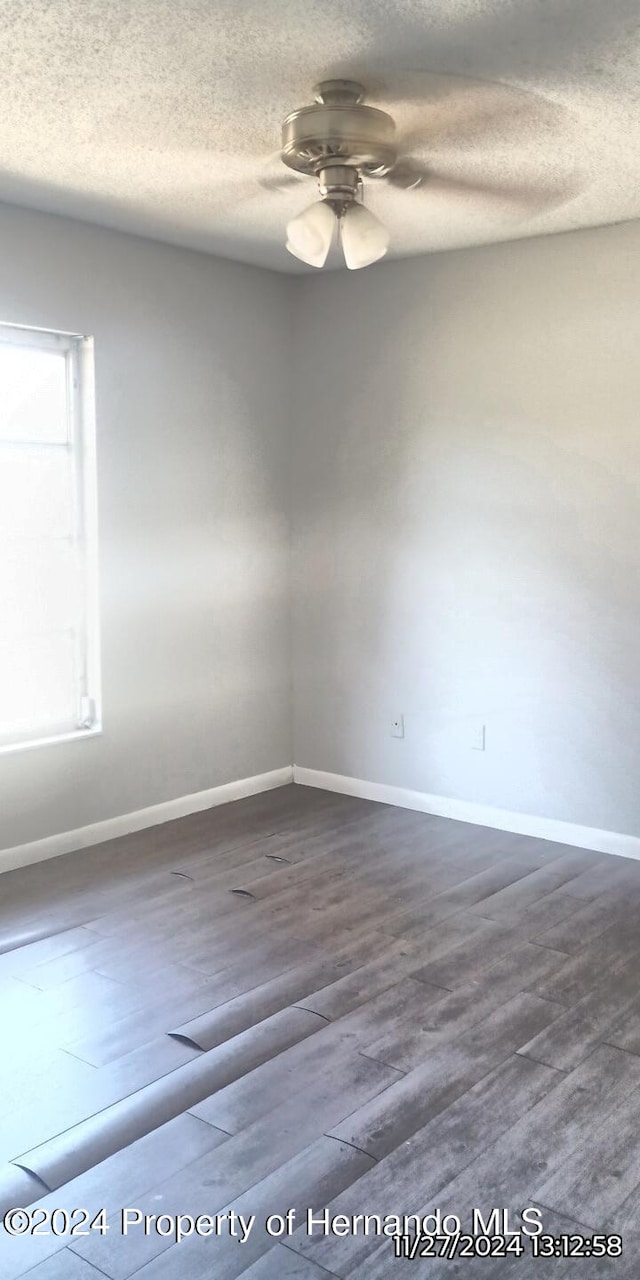 empty room with ceiling fan, wood-type flooring, and a textured ceiling