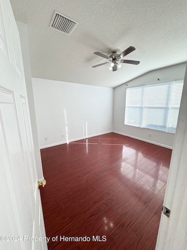 unfurnished room with ceiling fan, dark hardwood / wood-style flooring, a textured ceiling, and vaulted ceiling