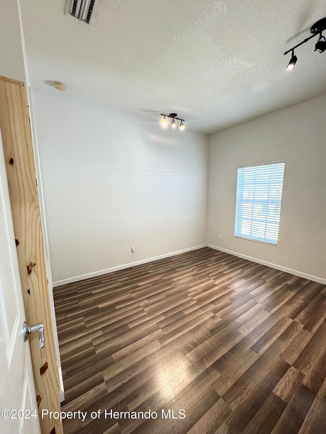 unfurnished room featuring a textured ceiling, dark hardwood / wood-style flooring, and track lighting