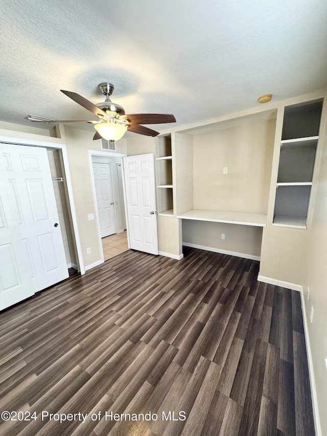 unfurnished bedroom featuring dark hardwood / wood-style floors, ceiling fan, built in desk, and a textured ceiling