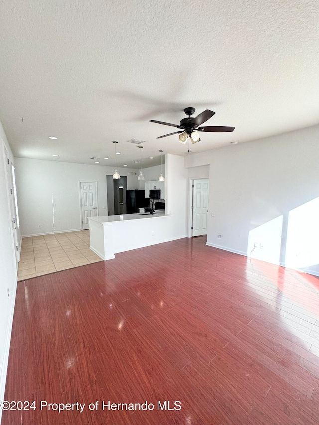 unfurnished living room with ceiling fan, light wood-type flooring, and a textured ceiling