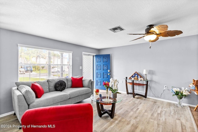 living room featuring ceiling fan, light wood-type flooring, and a textured ceiling