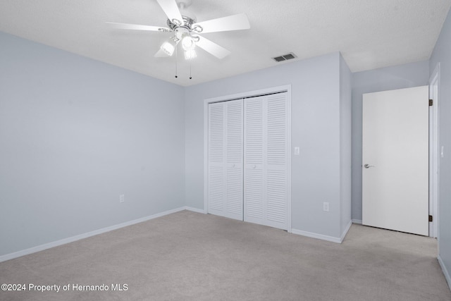 unfurnished bedroom featuring a textured ceiling, ceiling fan, light carpet, and a closet