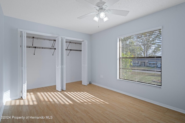 unfurnished bedroom featuring multiple closets, ceiling fan, a textured ceiling, and light wood-type flooring