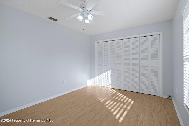 unfurnished bedroom featuring light wood-type flooring, a closet, multiple windows, and ceiling fan