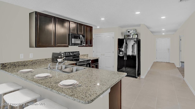 kitchen with a breakfast bar, black appliances, sink, light stone countertops, and kitchen peninsula