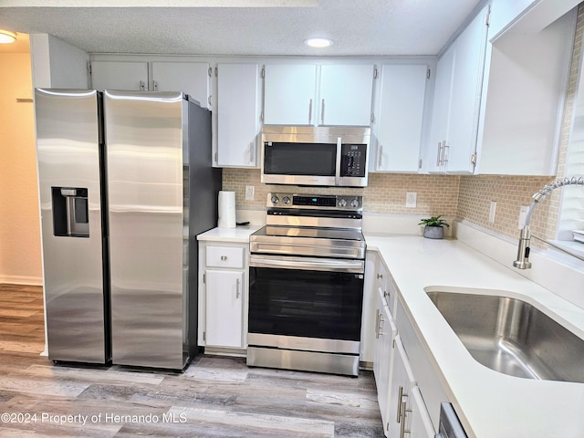 kitchen with appliances with stainless steel finishes, tasteful backsplash, sink, light hardwood / wood-style flooring, and white cabinetry