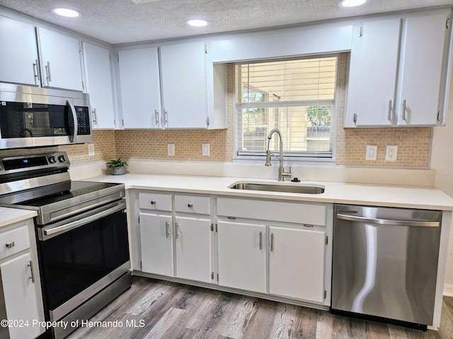 kitchen with white cabinets, appliances with stainless steel finishes, hardwood / wood-style flooring, and sink