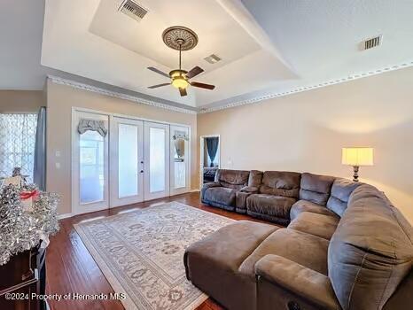 living room with dark hardwood / wood-style floors, ceiling fan, french doors, and a tray ceiling