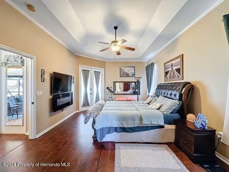 bedroom with a raised ceiling, ceiling fan, dark hardwood / wood-style flooring, and french doors