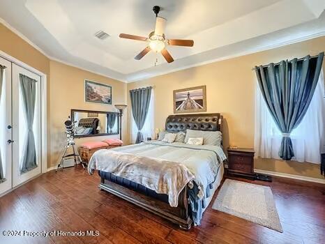 bedroom featuring french doors, a raised ceiling, ceiling fan, and dark wood-type flooring