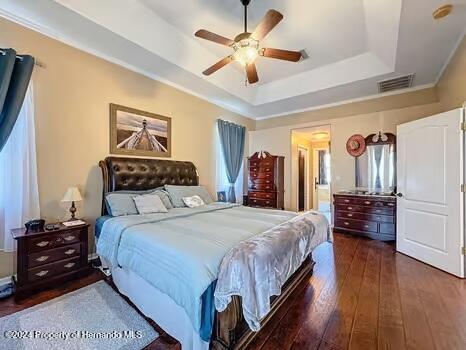 bedroom with dark hardwood / wood-style flooring, a tray ceiling, and ceiling fan