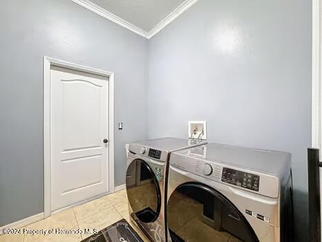 clothes washing area with washing machine and dryer, ornamental molding, and light tile patterned floors