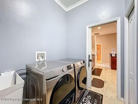 clothes washing area with sink, light tile patterned floors, washer and dryer, and ornamental molding