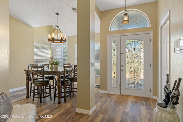 entrance foyer with dark wood-type flooring, a healthy amount of sunlight, a textured ceiling, and an inviting chandelier