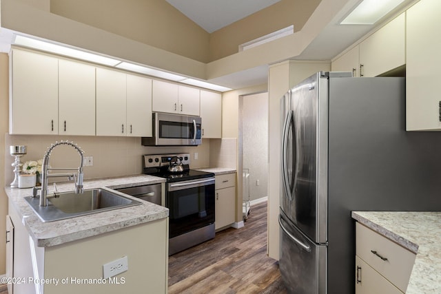 kitchen featuring decorative backsplash, appliances with stainless steel finishes, vaulted ceiling, sink, and hardwood / wood-style floors