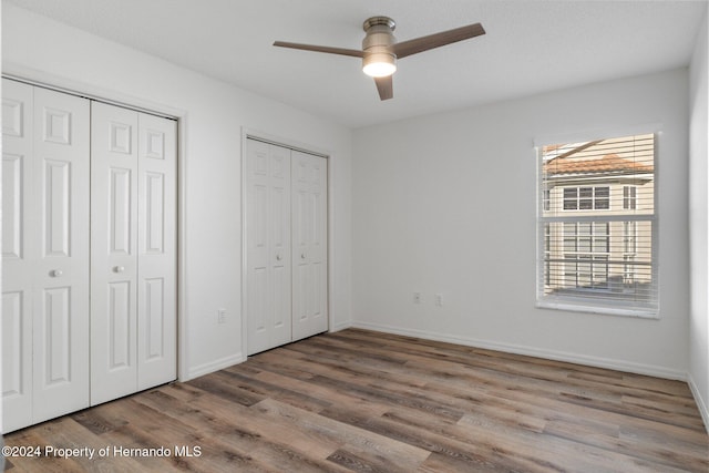 unfurnished bedroom featuring hardwood / wood-style floors, ceiling fan, and multiple closets