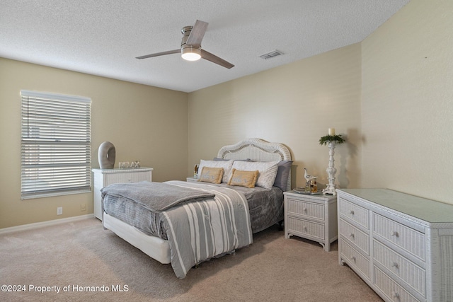 bedroom with a textured ceiling, light colored carpet, and ceiling fan