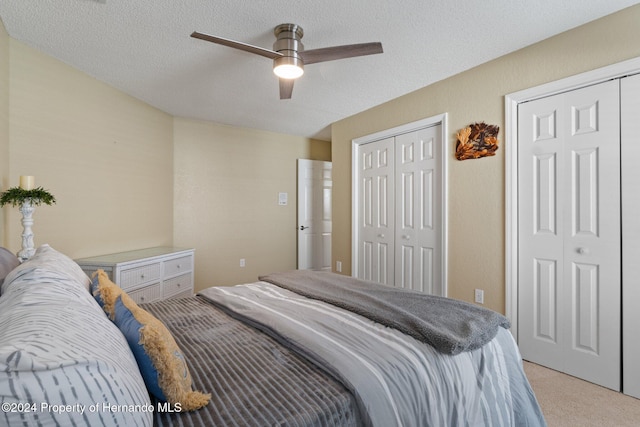 carpeted bedroom with ceiling fan, a textured ceiling, and two closets