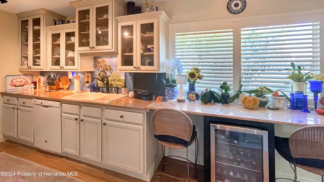 kitchen featuring light stone counters, white dishwasher, beverage cooler, sink, and light hardwood / wood-style flooring