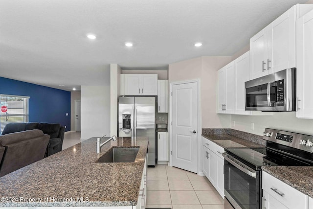 kitchen with white cabinetry, sink, dark stone counters, light tile patterned floors, and appliances with stainless steel finishes