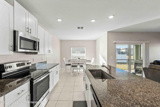 kitchen with stainless steel appliances, white cabinetry, and dark stone countertops