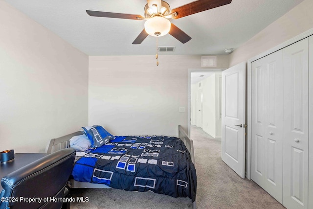 bedroom featuring ceiling fan, a closet, light colored carpet, and a textured ceiling