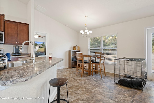 kitchen with lofted ceiling, ceiling fan with notable chandelier, sink, hanging light fixtures, and light stone countertops