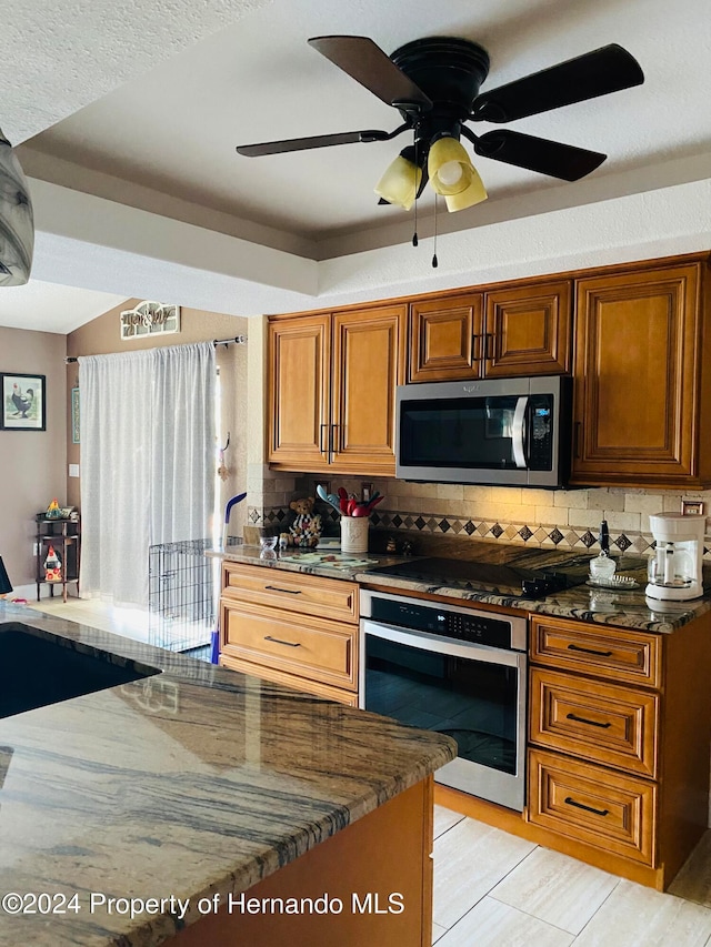 kitchen with backsplash, stainless steel appliances, ceiling fan, and dark stone counters