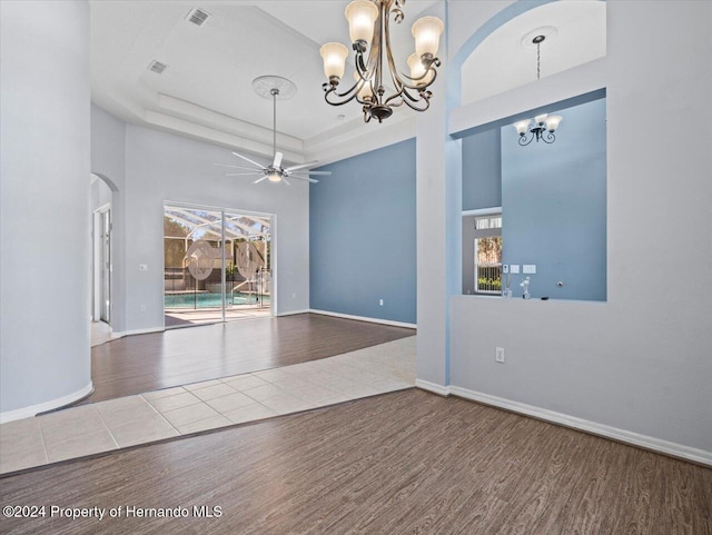 spare room with a tray ceiling, wood-type flooring, and ceiling fan with notable chandelier