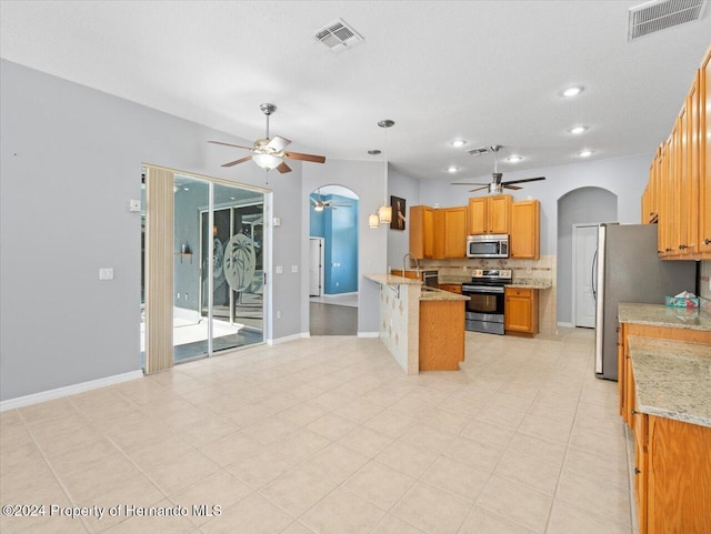 kitchen with tasteful backsplash, light stone counters, stainless steel appliances, sink, and hanging light fixtures