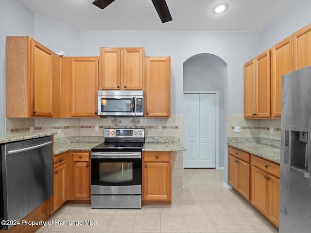 kitchen with a textured ceiling, light tile patterned flooring, light stone counters, and stainless steel appliances