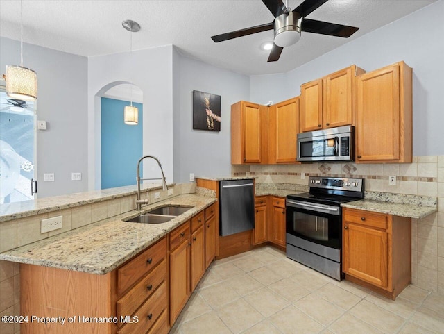 kitchen featuring kitchen peninsula, light stone counters, stainless steel appliances, sink, and decorative light fixtures